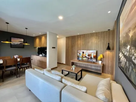 Modern open-plan living and dining area in a contemporary apartment with white sectional sofa, wooden accents, large wall art, and neutral tones. - Bali Villas